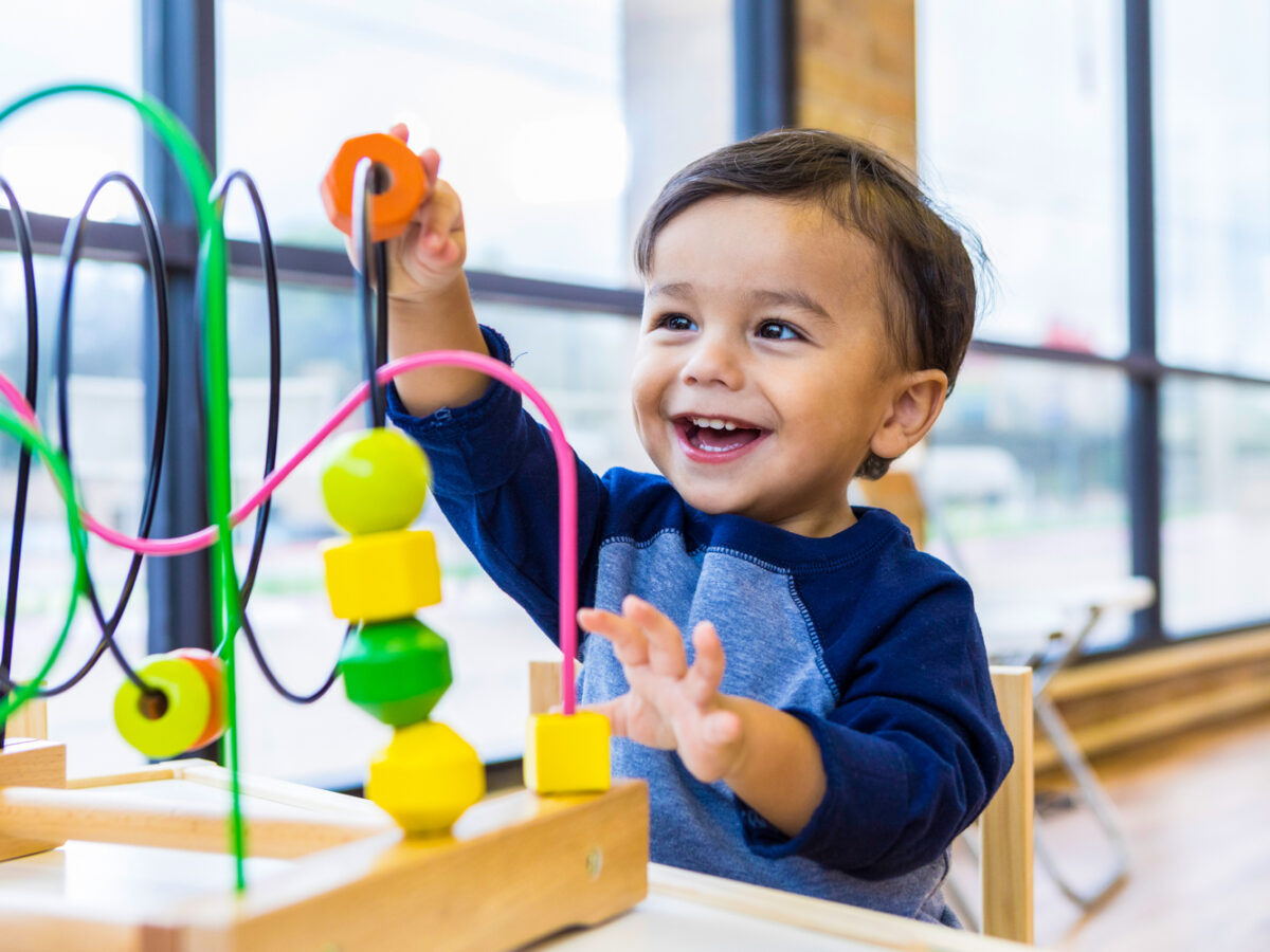 Toddler boy enjoys playing with toys in waiting room An adorable toddler boy sits at a table in a doctor's waiting room and reaches up cheerfully to play with a toy bead maze.